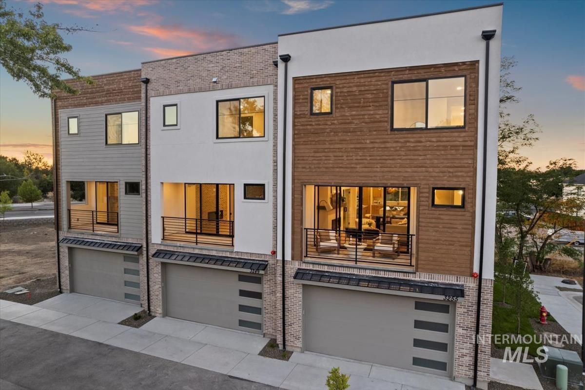 Back of house at dusk featuring a garage, a balcony, and concrete driveway