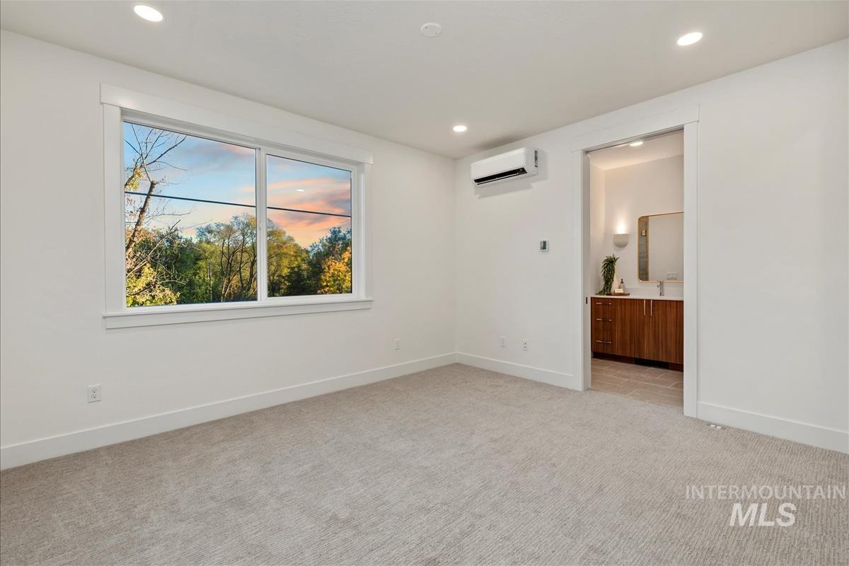Unfurnished bedroom featuring light carpet, recessed lighting, ensuite bathroom, and a wall mounted air conditioner