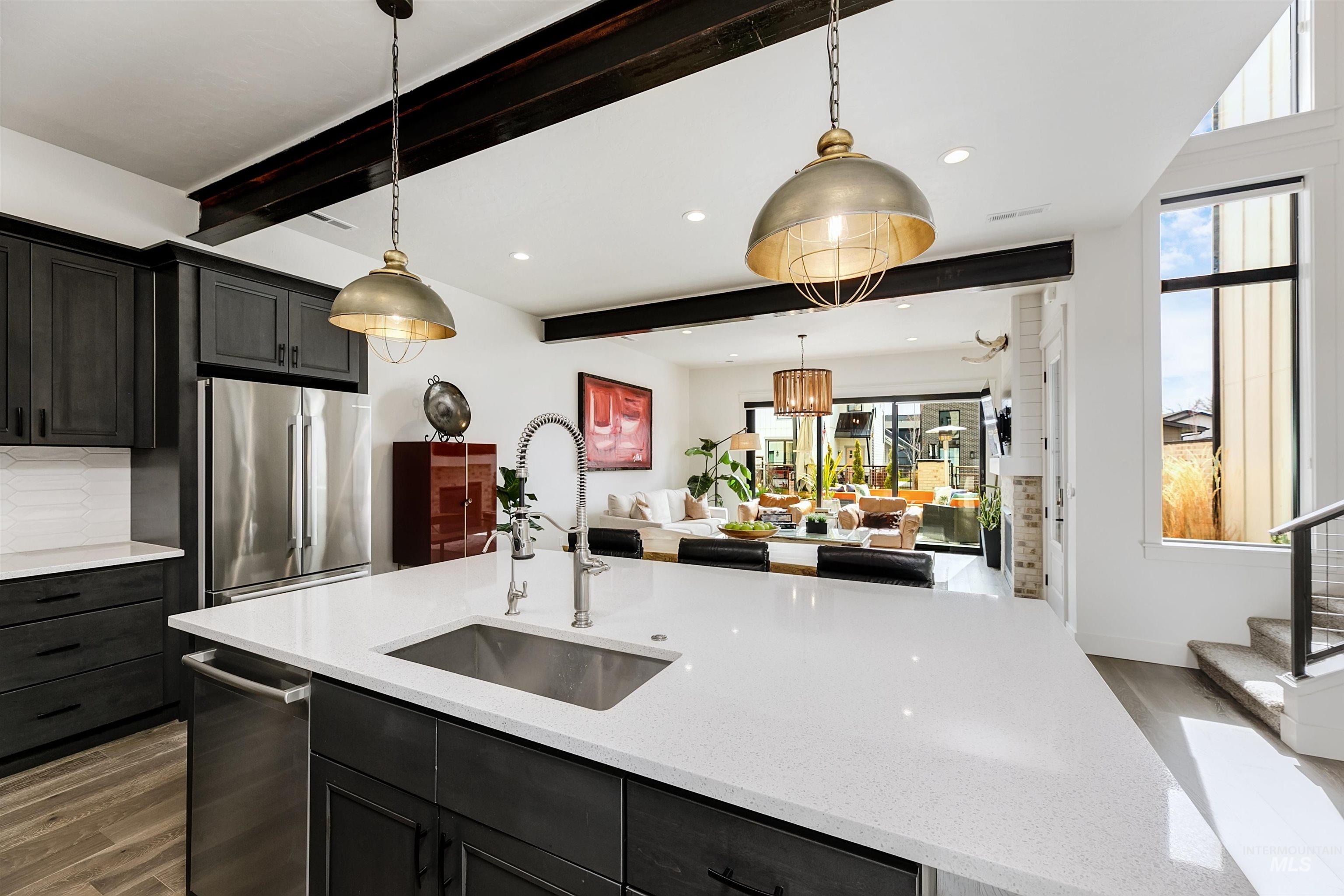 Kitchen featuring dark wood-style flooring, light stone countertops, pendant lighting, stainless steel appliances, and beam ceiling