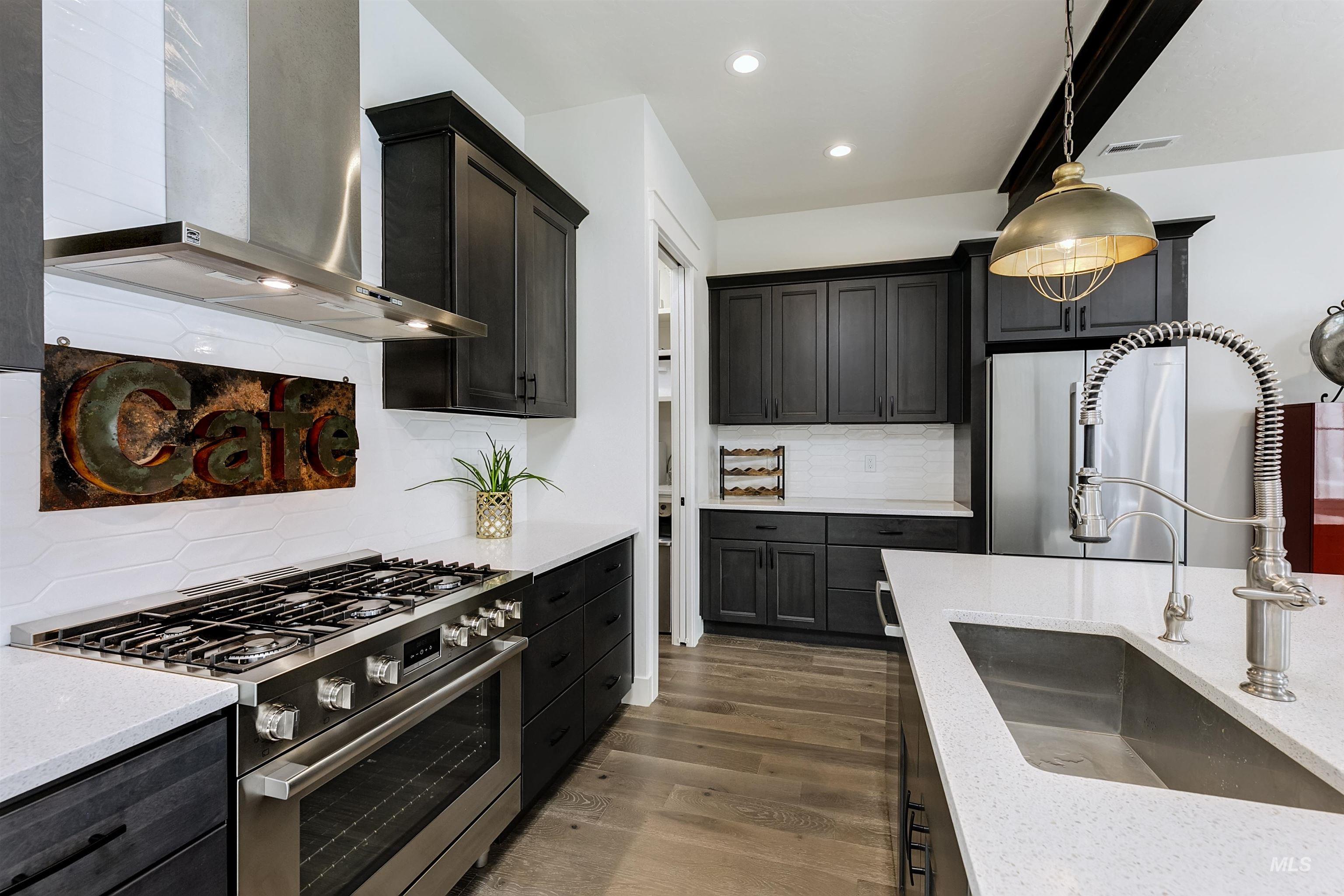 Kitchen with stainless steel appliances, tasteful backsplash, light wood-style floors, light stone counters, and decorative light fixtures