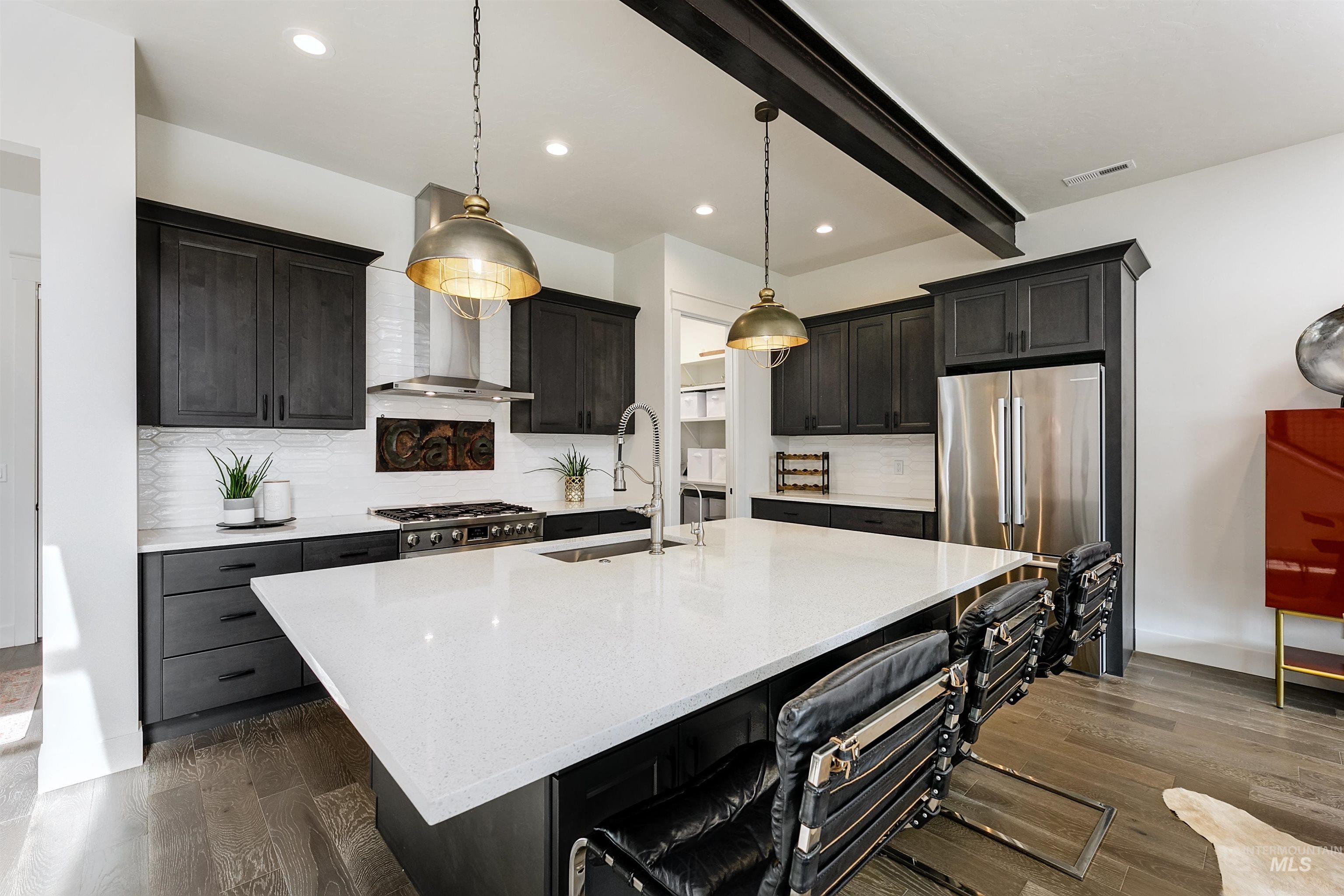 Kitchen featuring light stone counters, a center island with sink, a breakfast bar, dark wood-style flooring, and beam ceiling