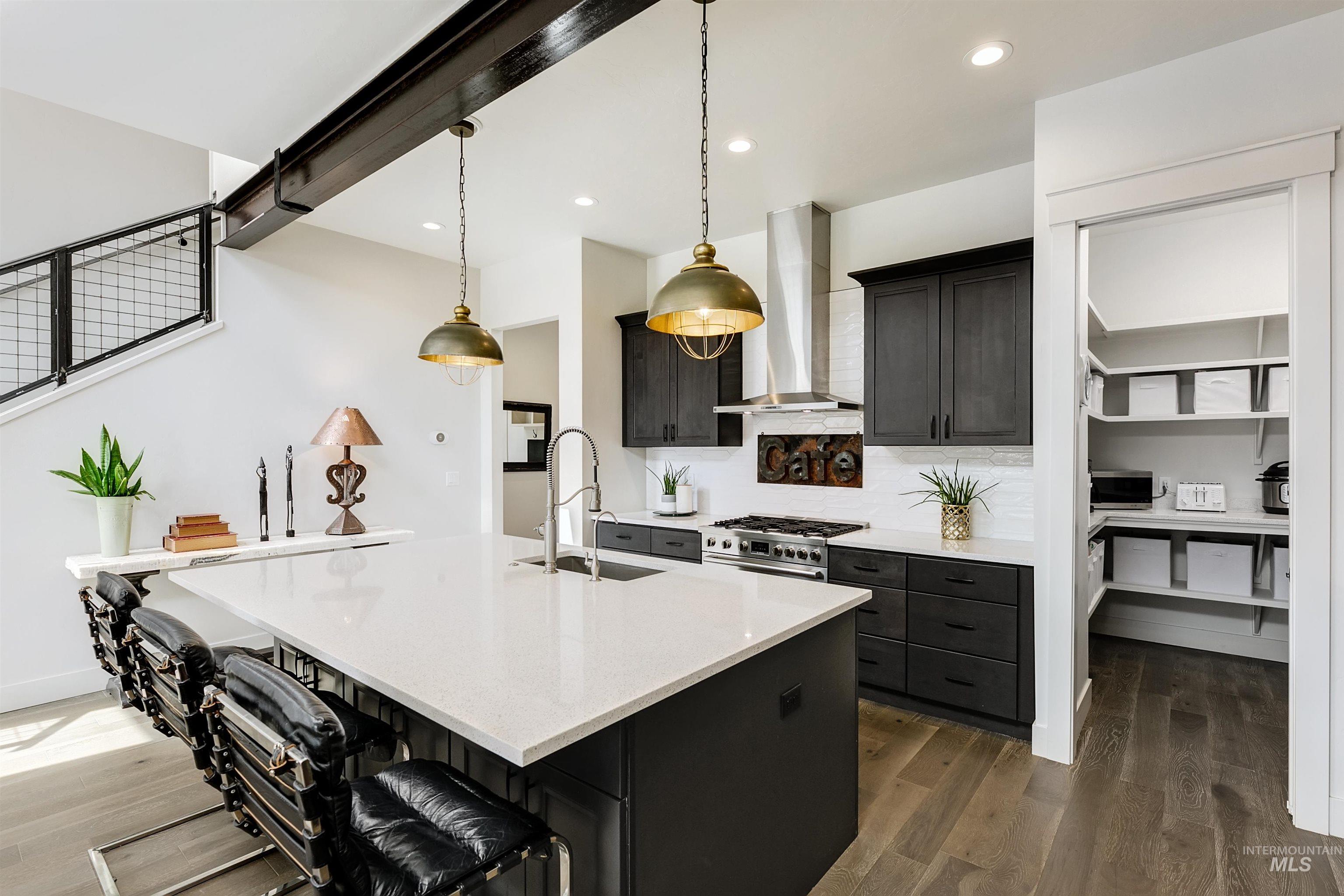 Kitchen featuring dark wood-type flooring, decorative light fixtures, a center island with sink, light stone countertops, and a kitchen breakfast bar