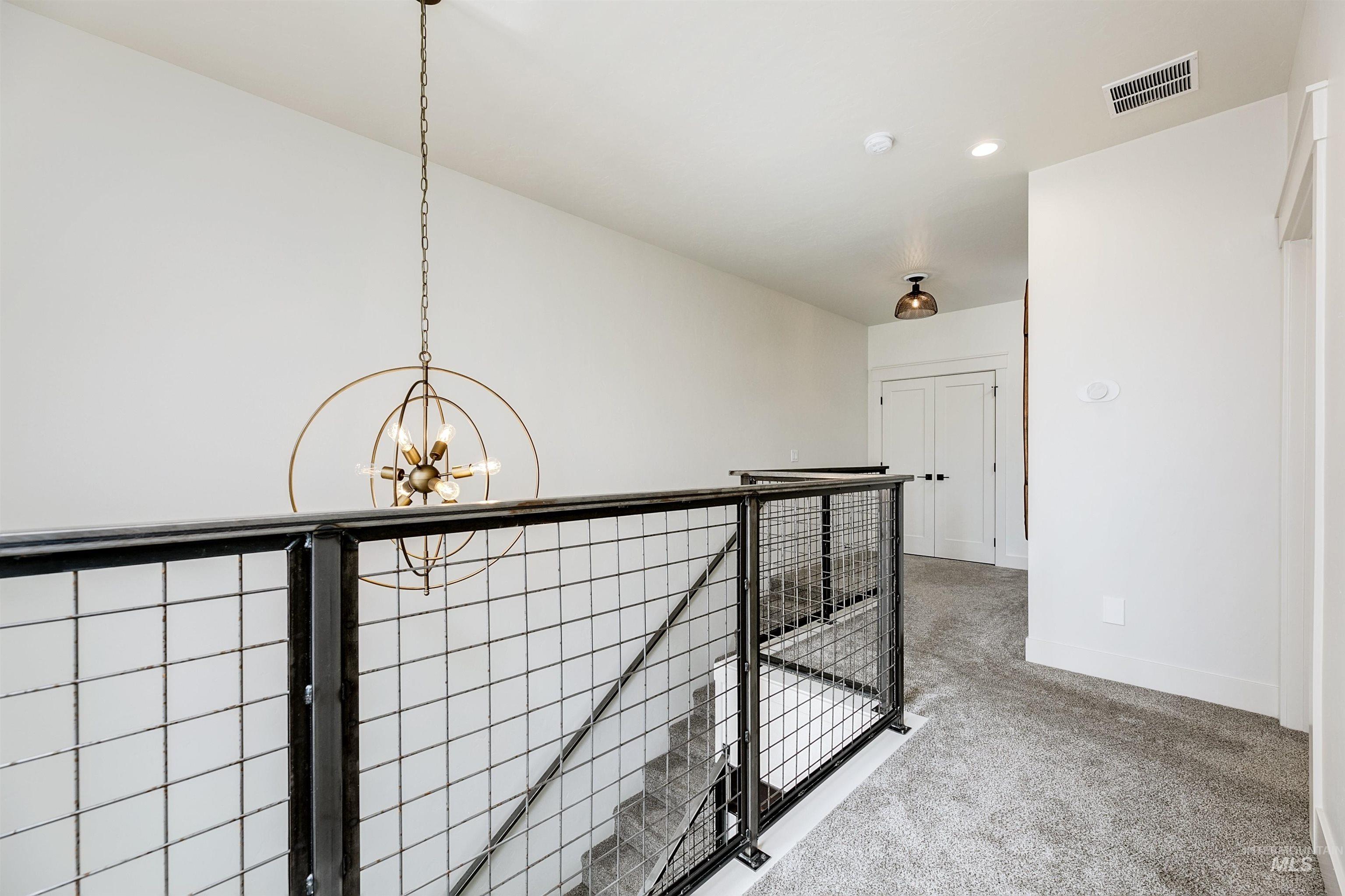 Corridor with an upstairs landing, carpet flooring, and suspended lighting