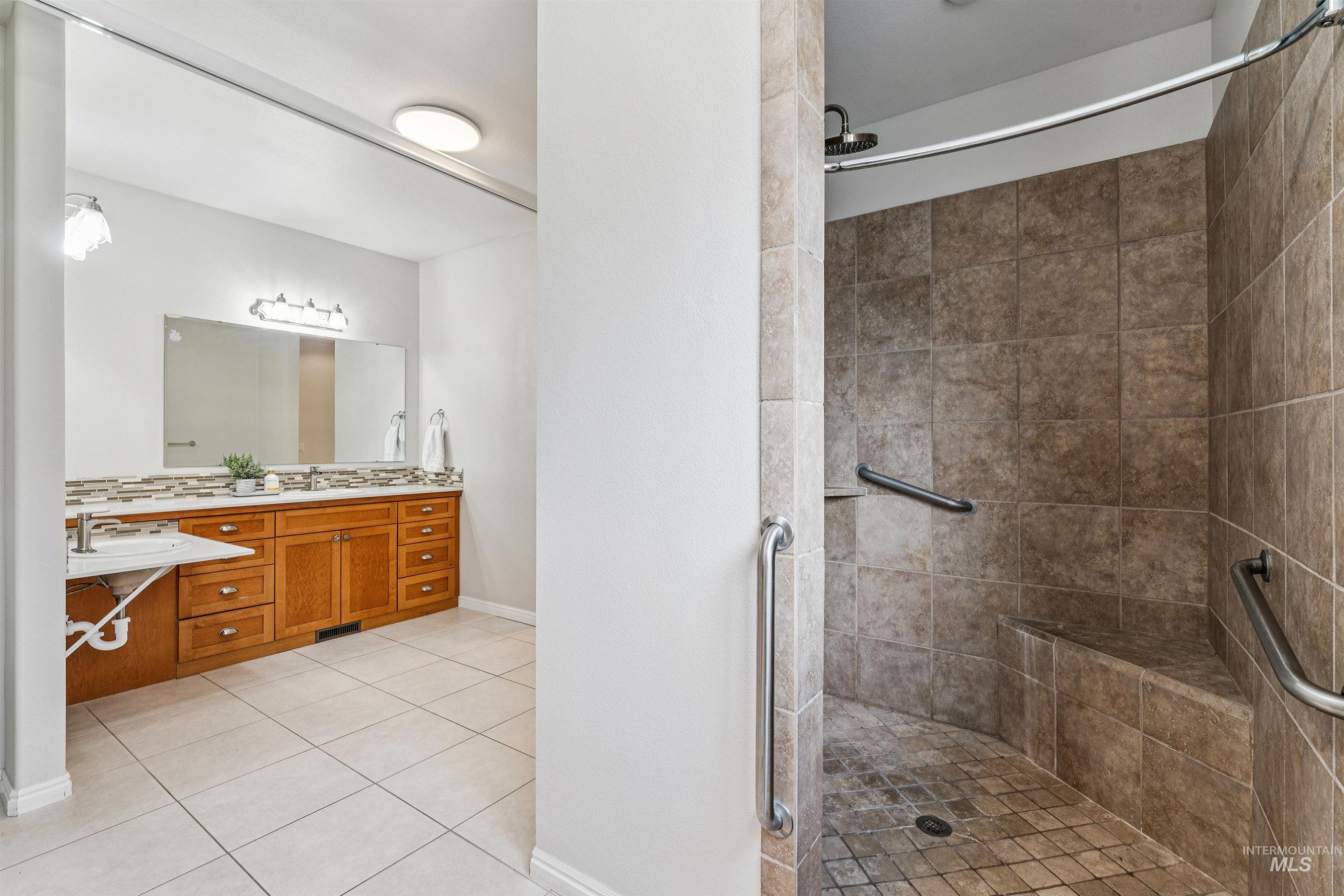 Full bathroom featuring double vanity, tiled shower, and light tile patterned floors