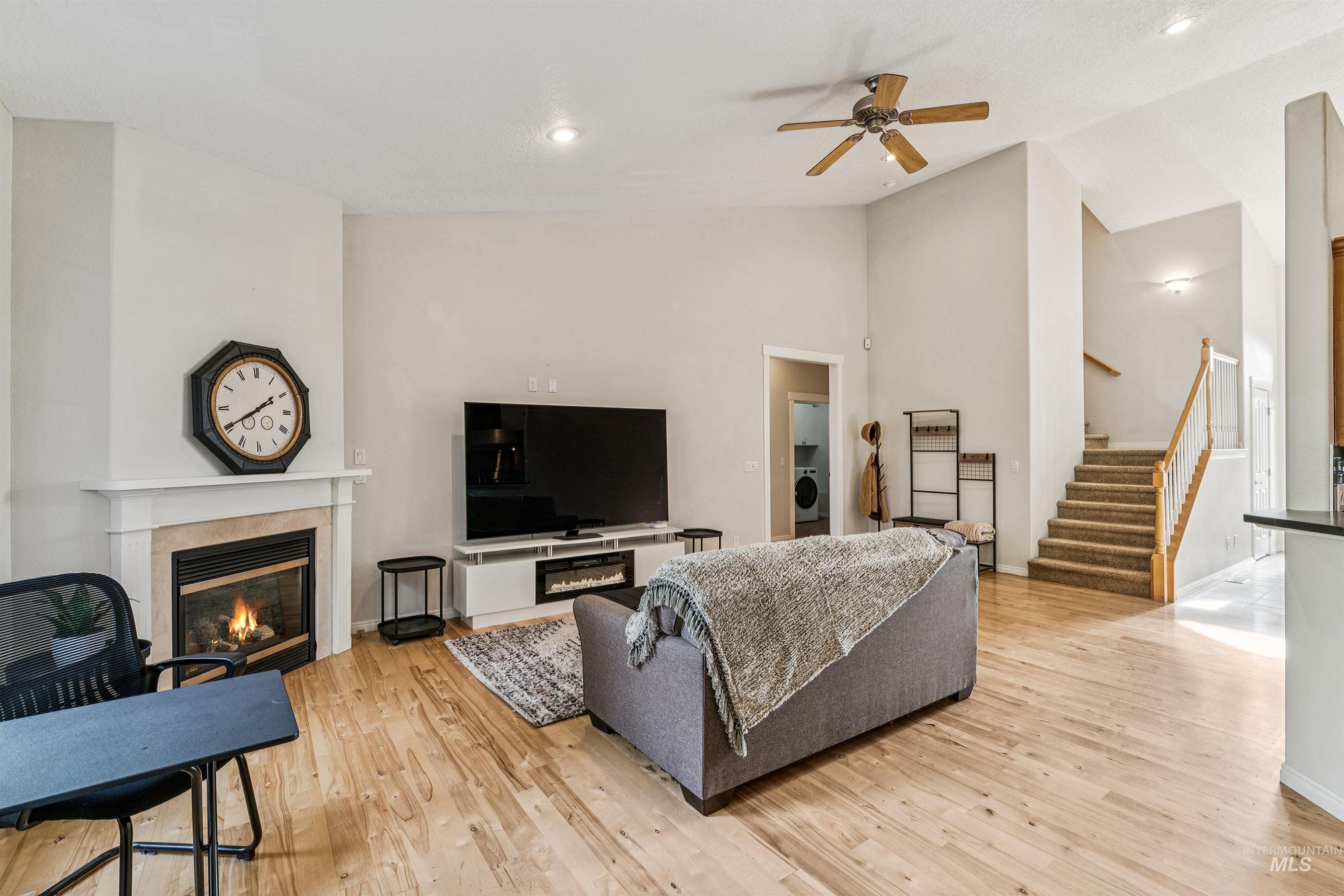 Living area with stairs, a tiled fireplace, light wood-type flooring, washer / clothes dryer, and ceiling fan