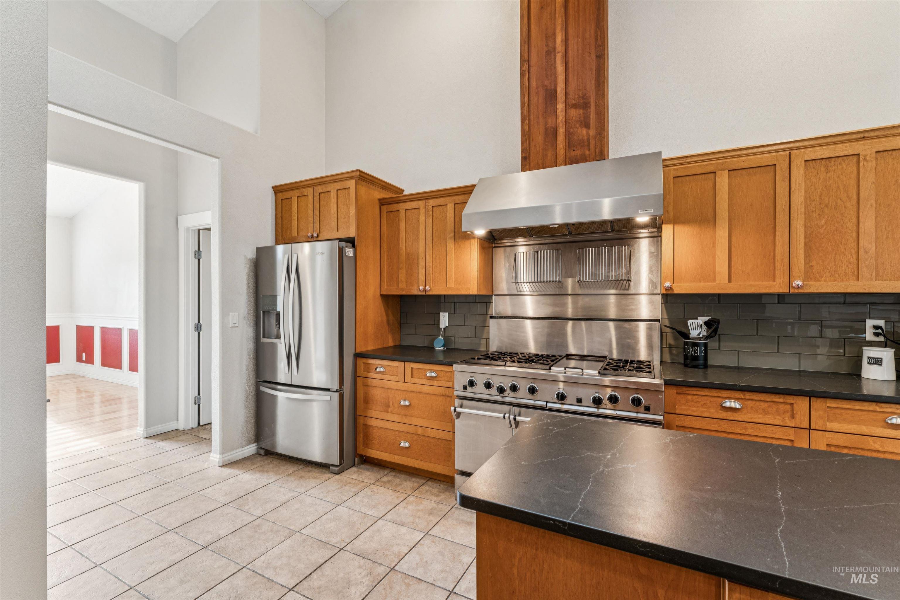 Kitchen with brown cabinets, stainless steel appliances, a high ceiling, light tile patterned floors, and decorative backsplash