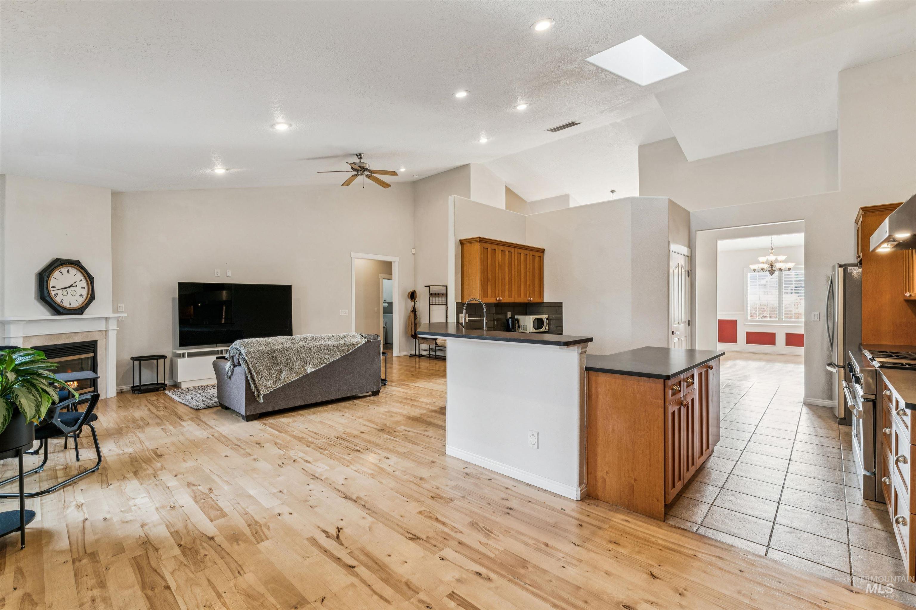Kitchen with brown cabinets, dark countertops, a tile fireplace, high vaulted ceiling, and stainless steel appliances