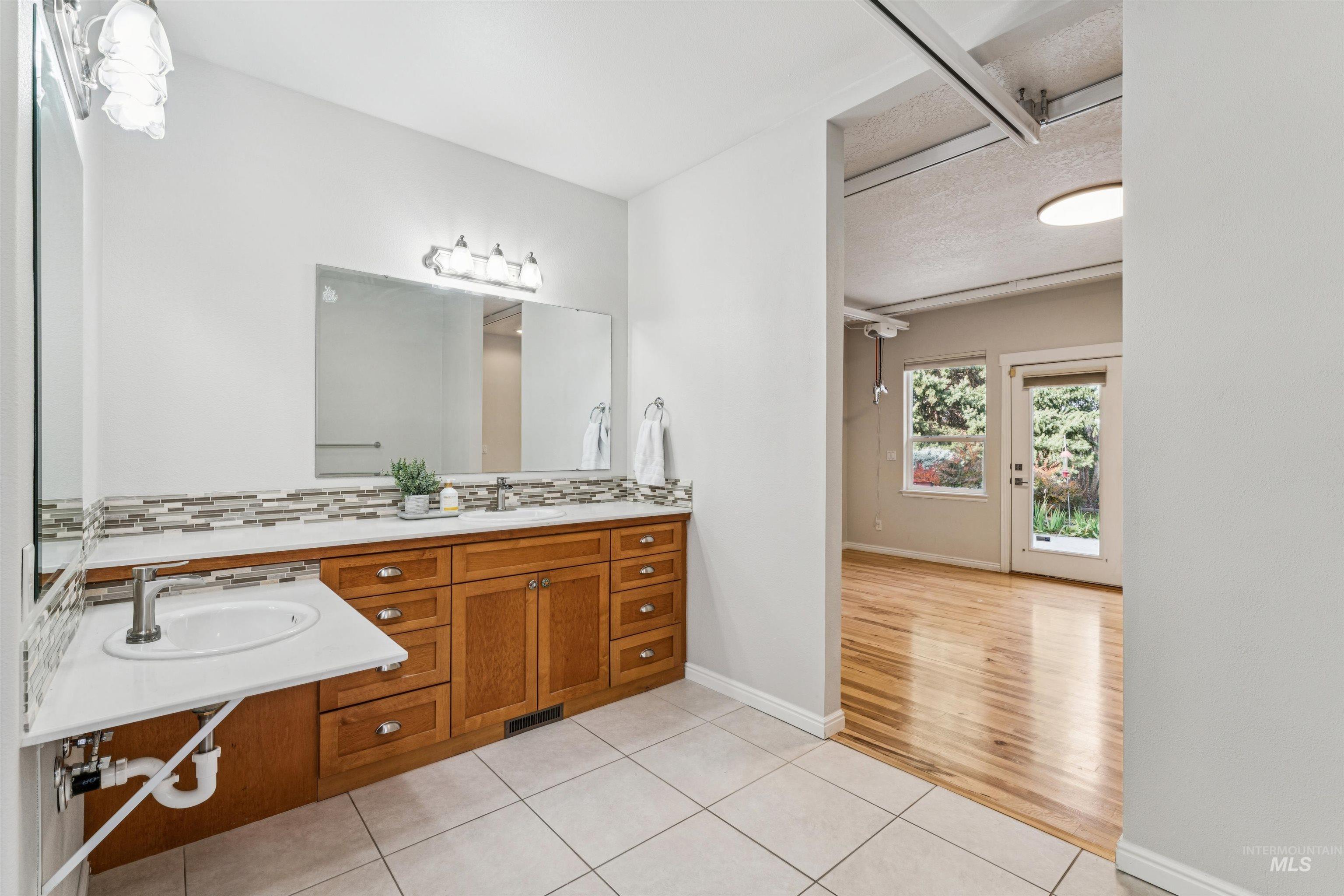 Bathroom with light tile patterned flooring, double vanity, decorative backsplash, and a textured ceiling