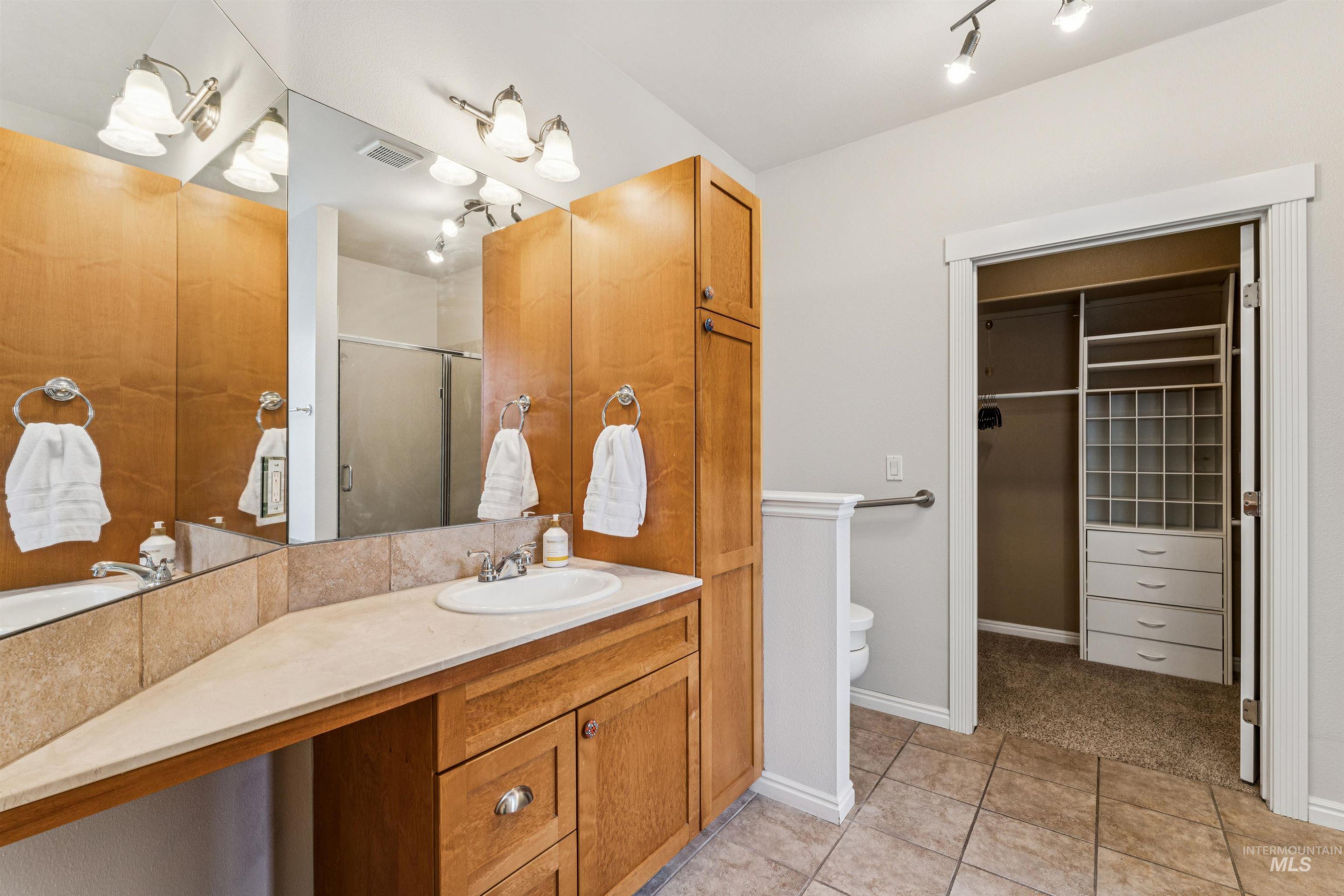 Bathroom with vanity, a shower stall, a walk in closet, and light tile patterned flooring