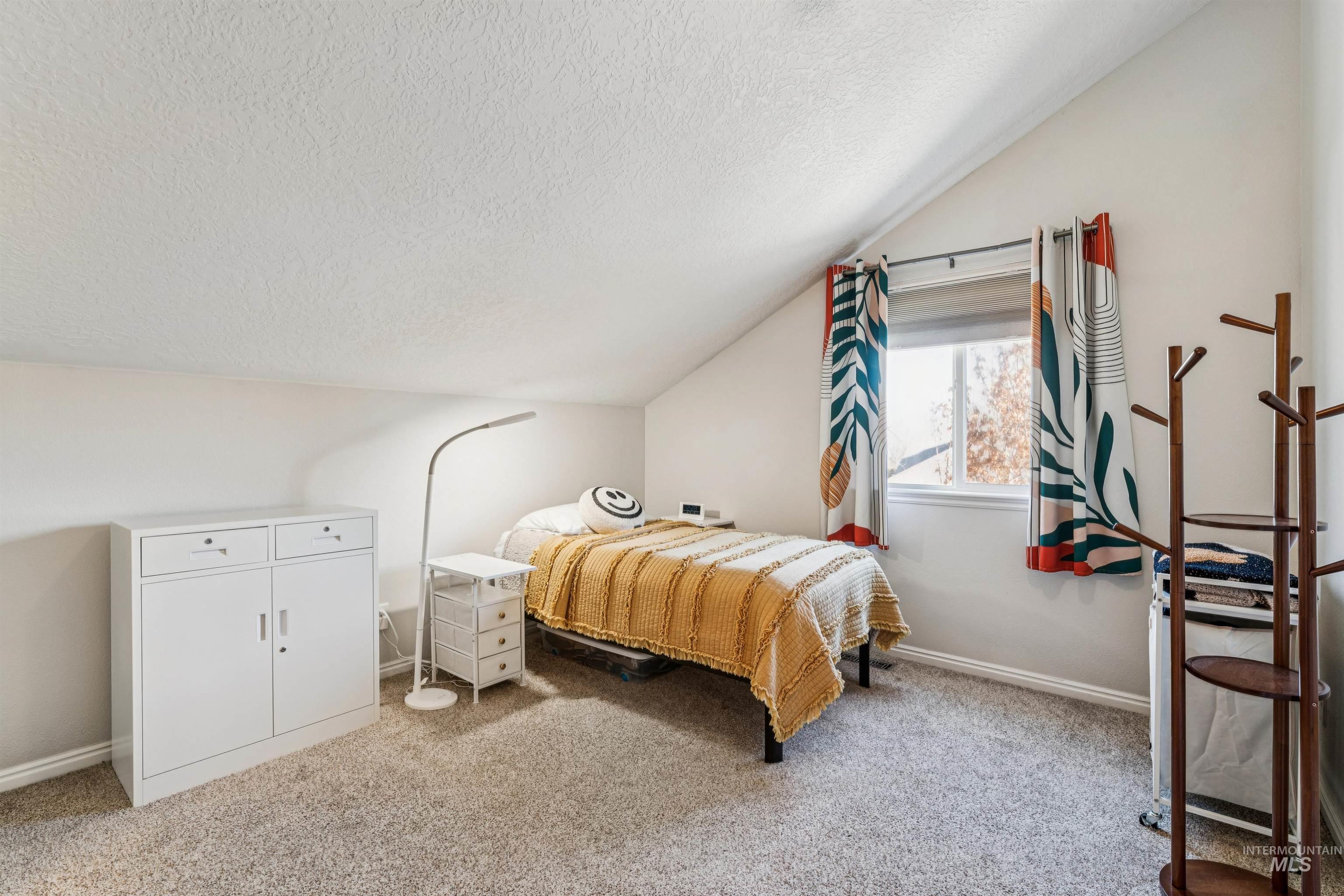 Bedroom featuring vaulted ceiling, a textured ceiling, and light colored carpet