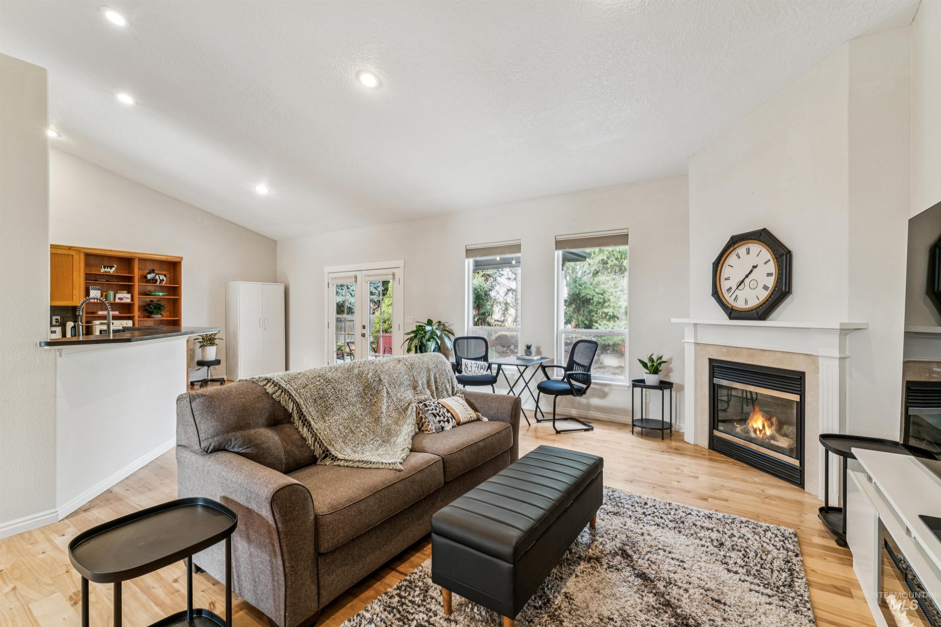 Living room with a fireplace, light wood-style floors, recessed lighting, french doors, and vaulted ceiling