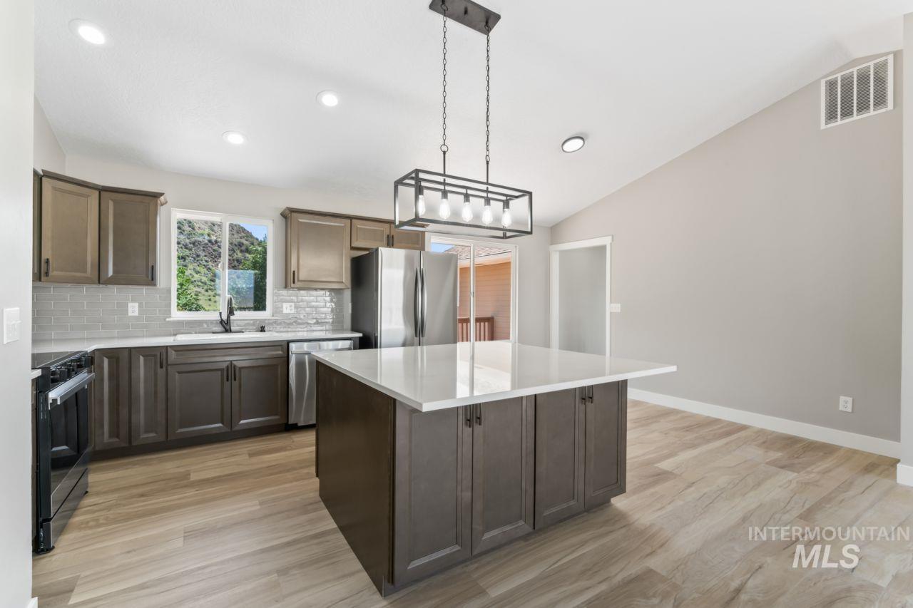 Kitchen with stainless steel appliances, tasteful backsplash, a center island, light wood-type flooring, and lofted ceiling