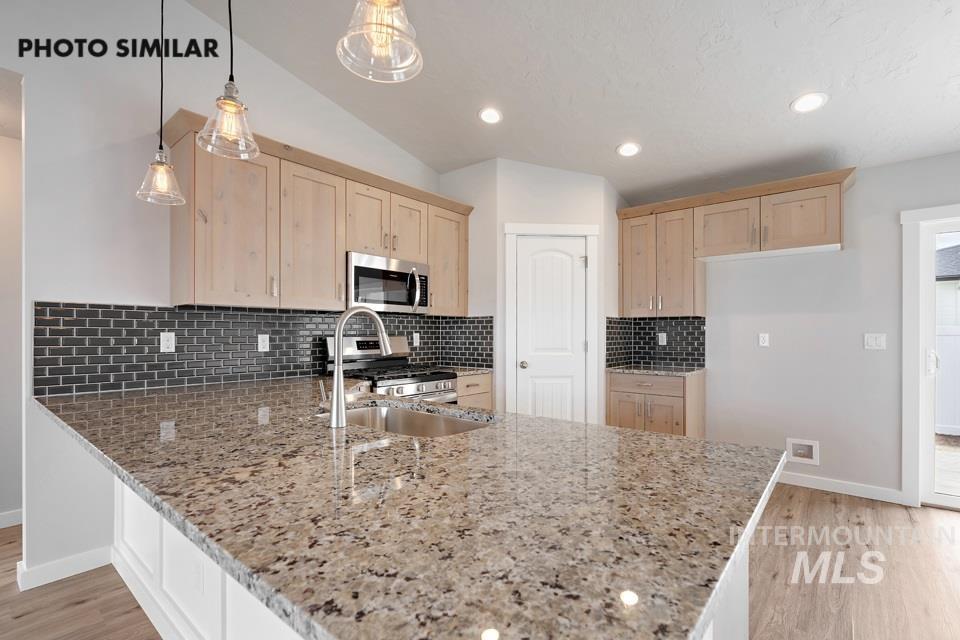 Kitchen featuring light brown cabinetry, light wood-type flooring, lofted ceiling, a peninsula, and light stone counters