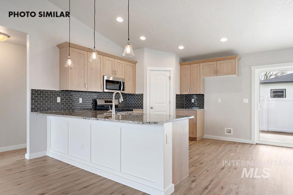 Kitchen featuring light brown cabinets, light stone counters, a peninsula, light wood-style floors, and appliances with stainless steel finishes
