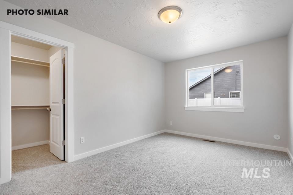 Unfurnished bedroom with carpet flooring, a walk in closet, and a textured ceiling