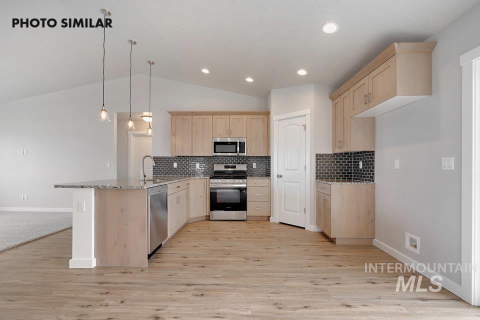 Kitchen featuring light brown cabinetry, a peninsula, stainless steel appliances, light wood-type flooring, and lofted ceiling