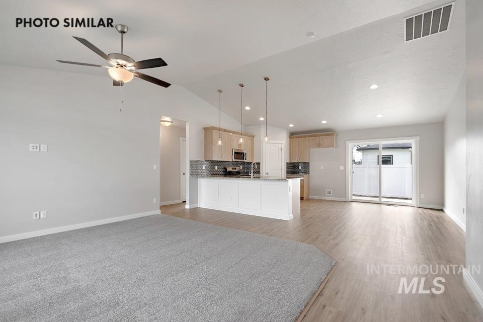Kitchen featuring open floor plan, light wood-type flooring, lofted ceiling, decorative backsplash, and ceiling fan