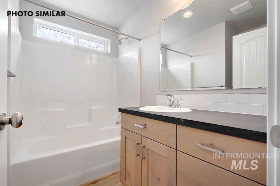 Full bath with vanity, bathtub / shower combination, backsplash, and wood finished floors