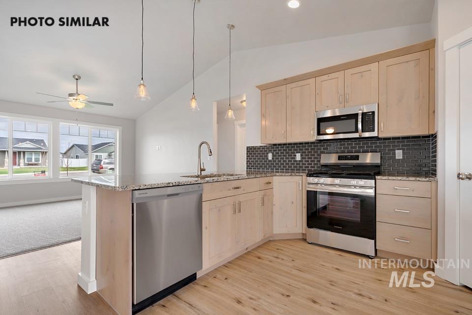 Kitchen with light brown cabinetry, vaulted ceiling, a peninsula, stainless steel appliances, and backsplash