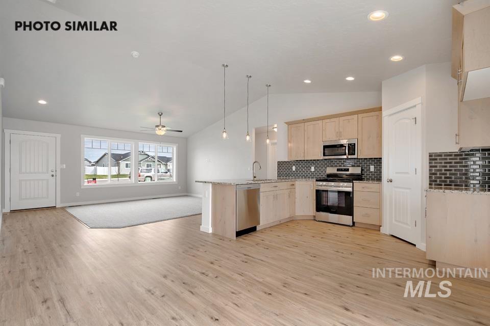 Kitchen with vaulted ceiling, light brown cabinetry, a peninsula, backsplash, and open floor plan
