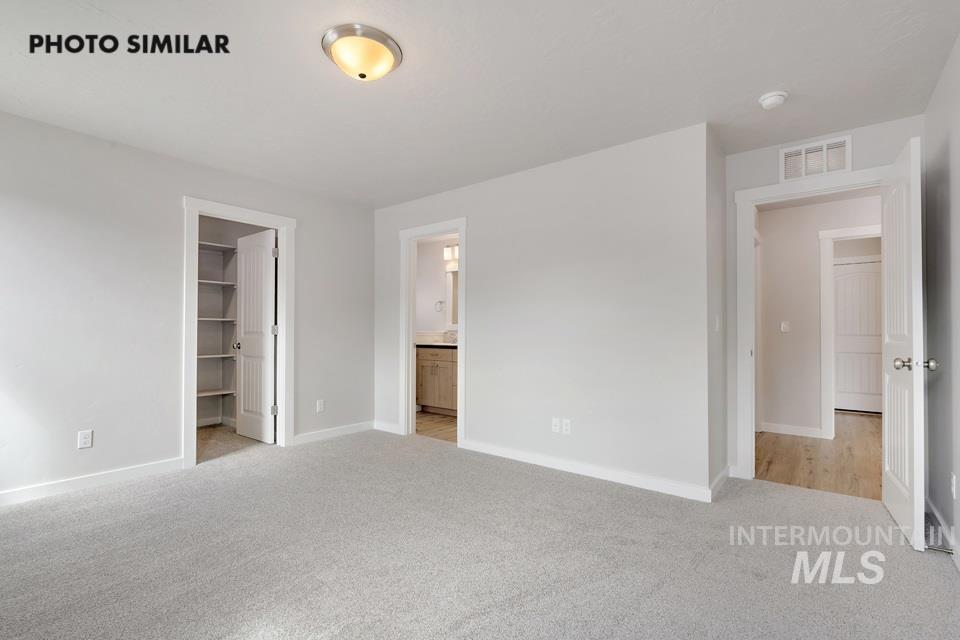 Unfurnished bedroom featuring light carpet, a walk in closet, and ensuite bathroom