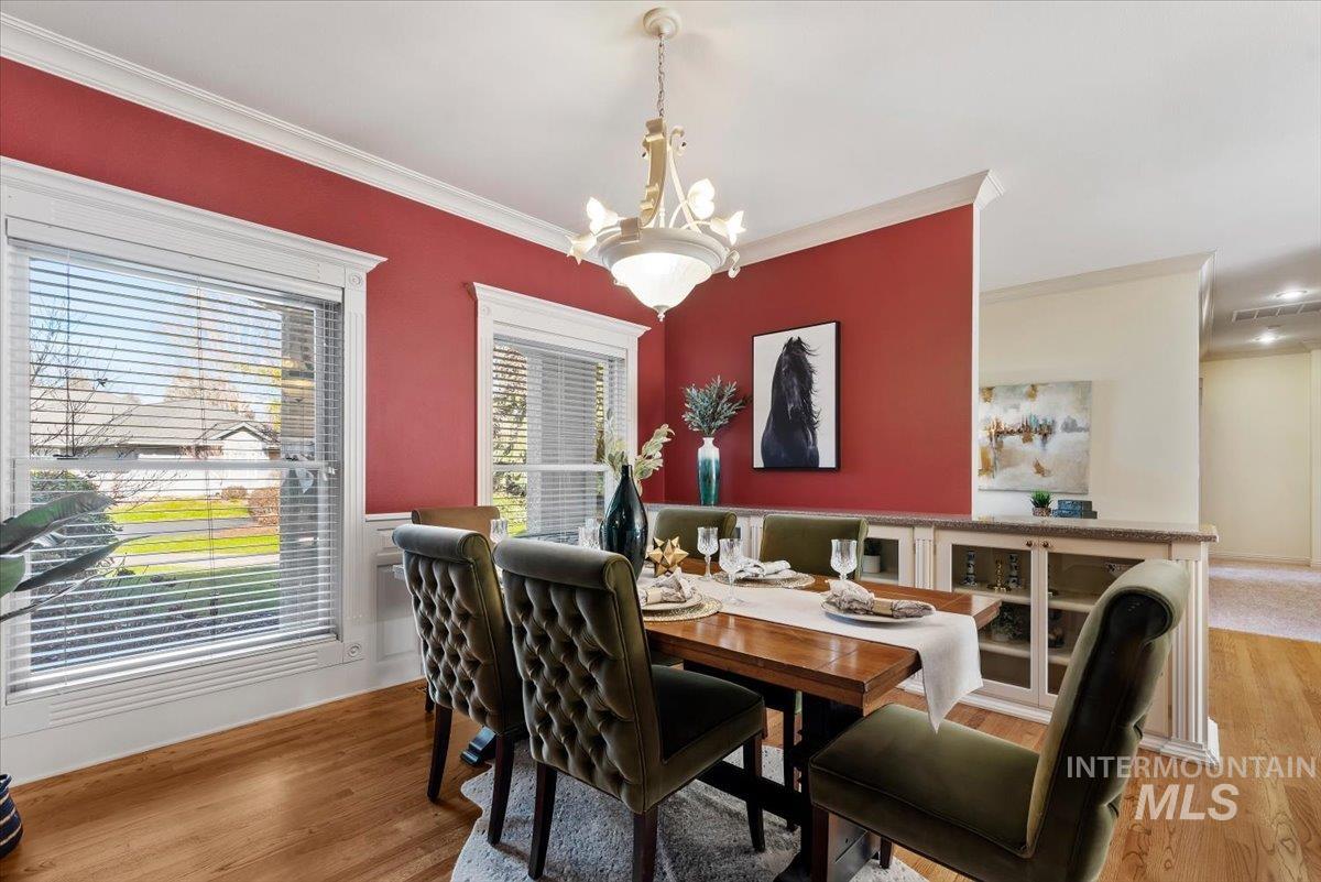 Dining area with light wood-style floors, ornamental molding, and suspended lighting