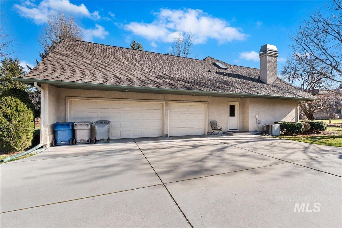 Back of house featuring stucco siding, a chimney, an attached garage, concrete driveway, and a shingled roof