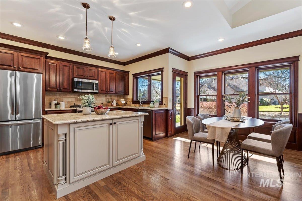 Two tone kitchen with stainless steel appliances, two tone cabinetry, light wood-style floors, ornamental molding, and light stone counters