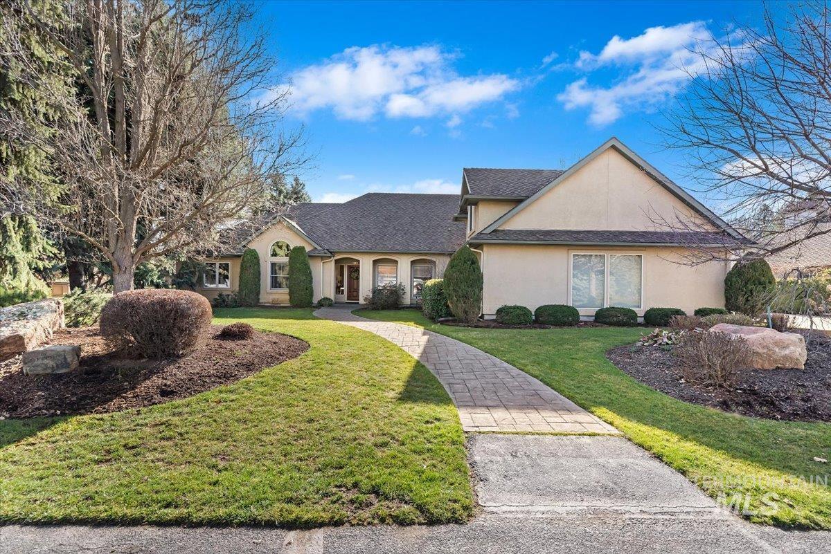 View of front of home with stucco siding, a front yard, and a shingled roof