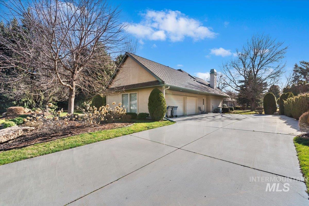 View of side of home featuring stucco siding, a garage, driveway, and a chimney