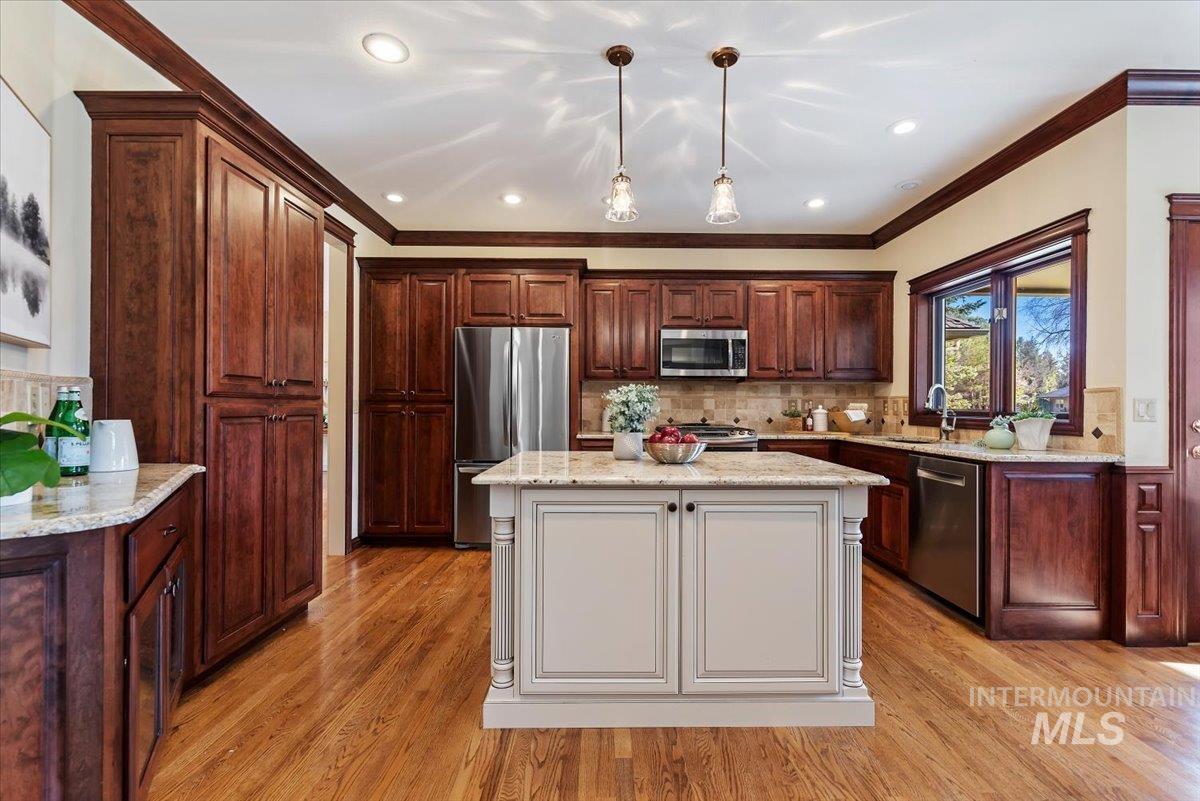 Two tone kitchen featuring dual tone cabinetry, stainless steel appliances, light stone countertops, a kitchen island, and light wood finished floors