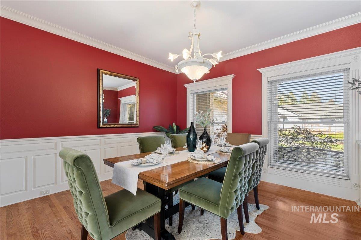 Dining space featuring crown molding, wood finished floors, suspended lighting, a wainscoted wall, and a decorative wall