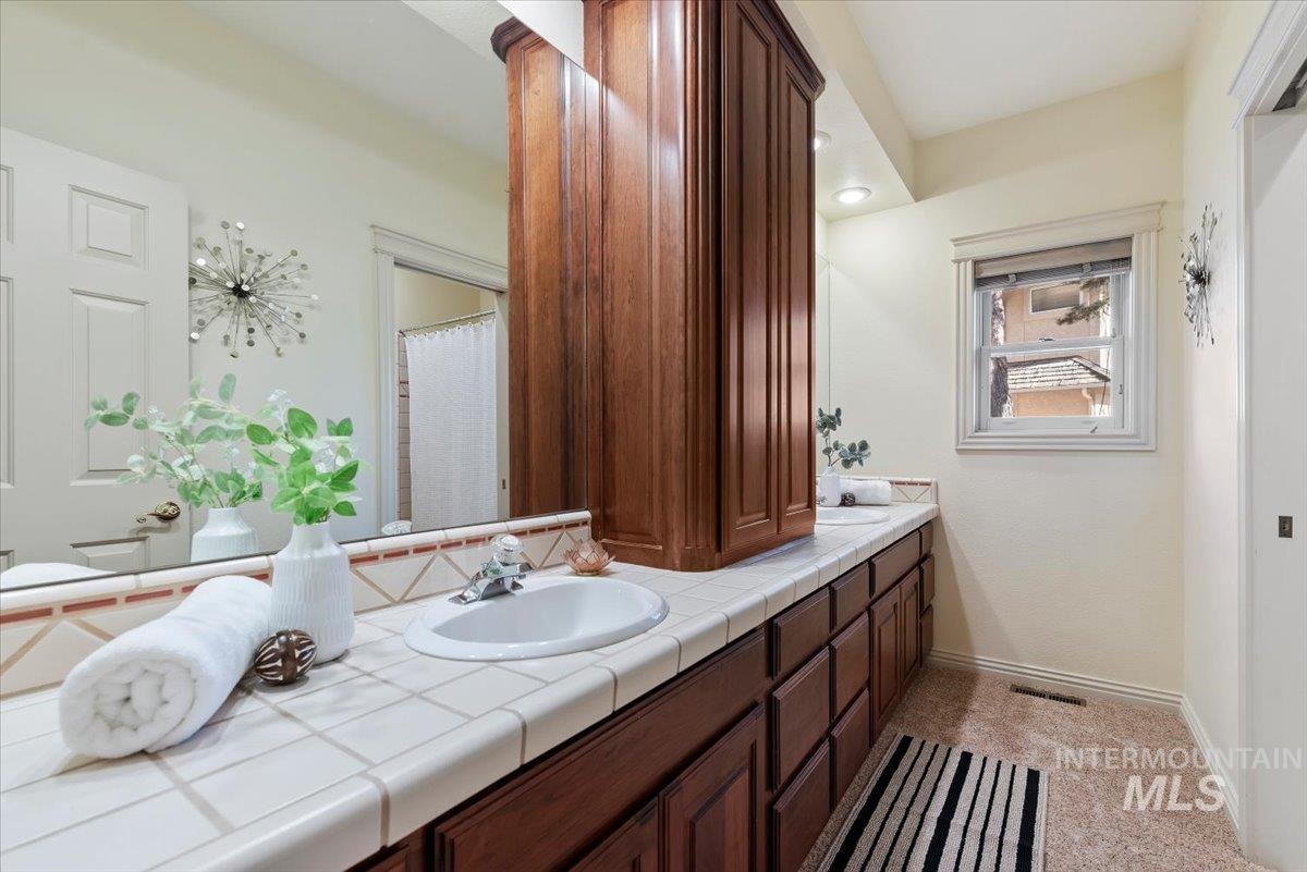 Bathroom with double vanity, light colored carpet, and a shower with curtain