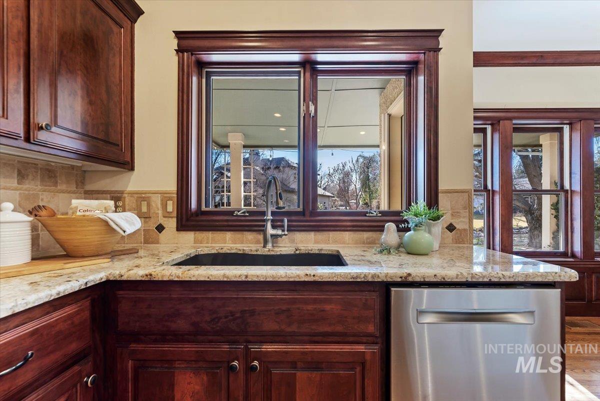 Kitchen with dishwasher, light stone counters, and dark wood finish cabinets