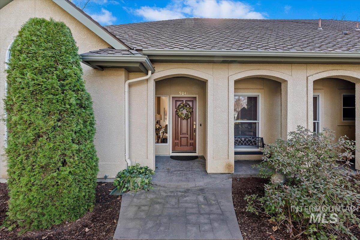 Doorway to property with a shingled roof and stucco siding