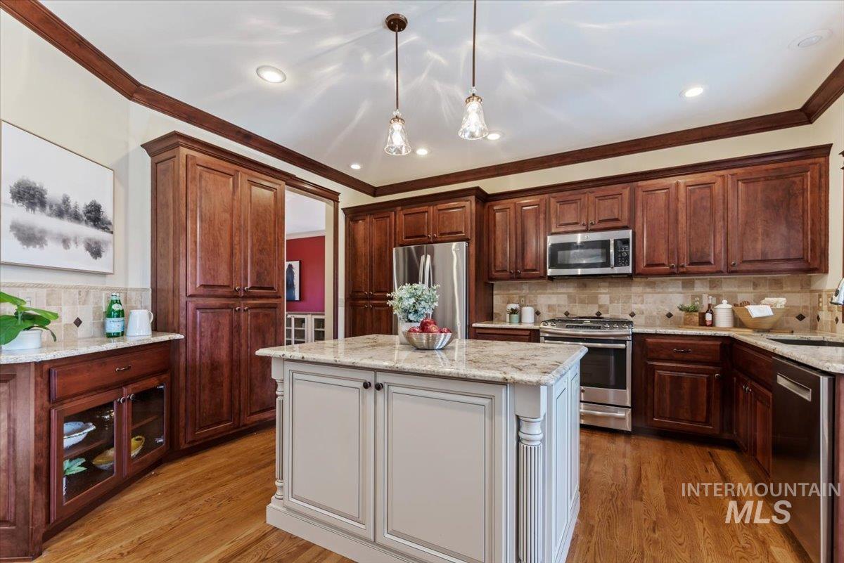 Dual tone kitchen with dual tone cabinetry, stainless steel appliances, light stone countertops, light wood-type flooring, and backsplash