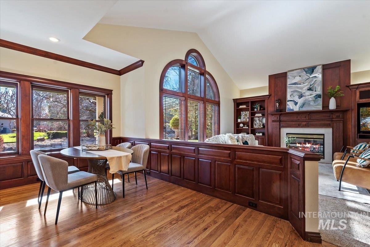 Dining room with vaulted ceiling, a glass covered fireplace, a wainscoted wall, light wood-style floors, and crown molding