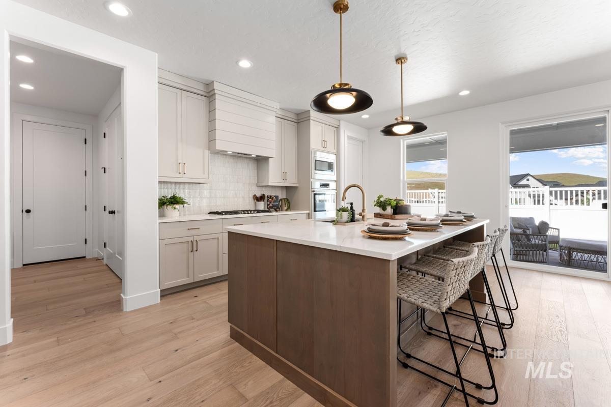 Modern kitchen featuring a large center island with seating, light wood-finish flooring, white cabinetry, a built-in oven, and recessed lighting