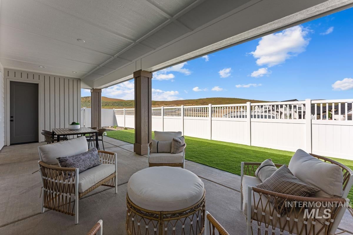 Covered concrete patio featuring board-and-batten siding, large support columns with wood-finish trim, a manicured lawn, and a white picket fence
