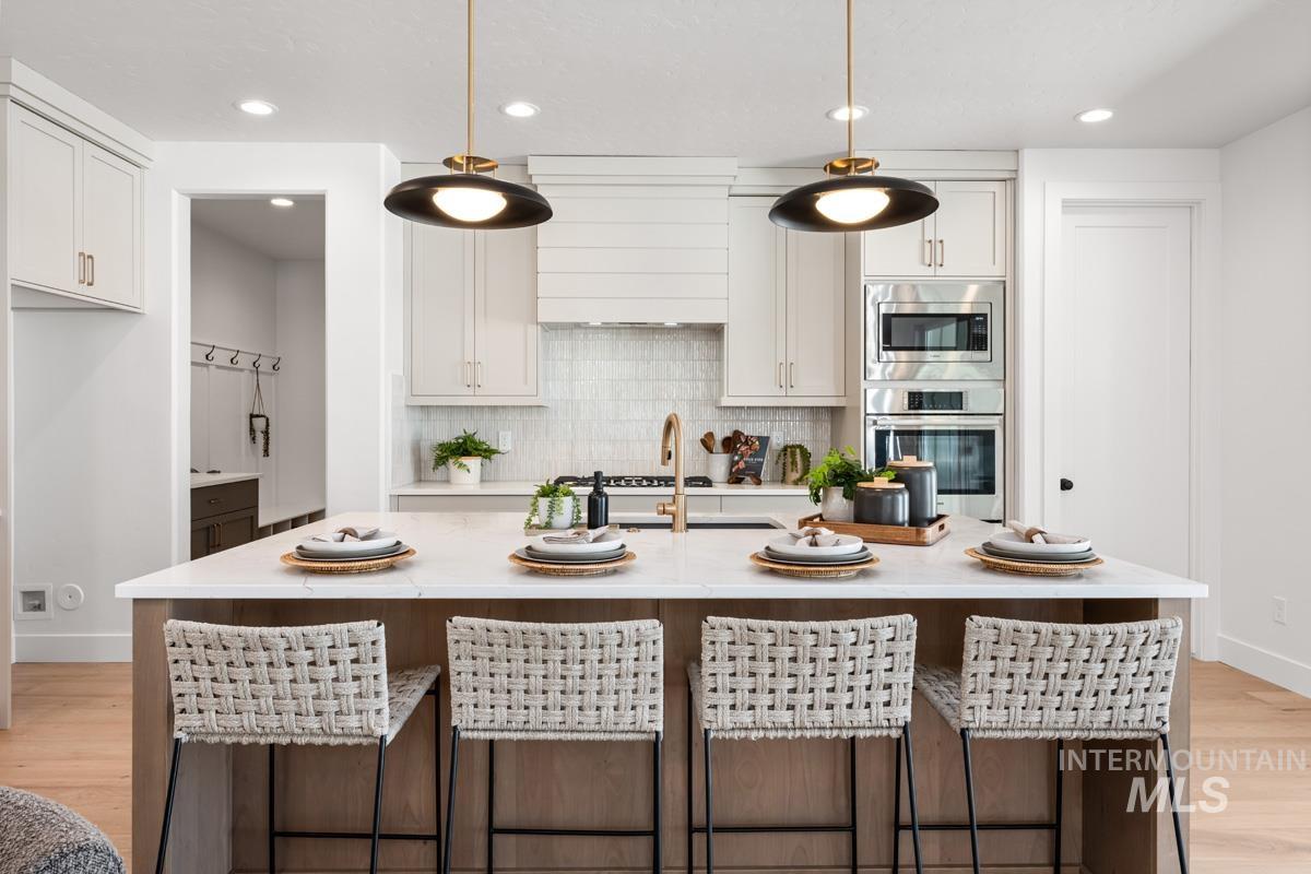 Kitchen featuring a central island with countertop seating, light wood-finish flooring, white cabinetry, integrated stainless steel appliances, and a shiplap range hood