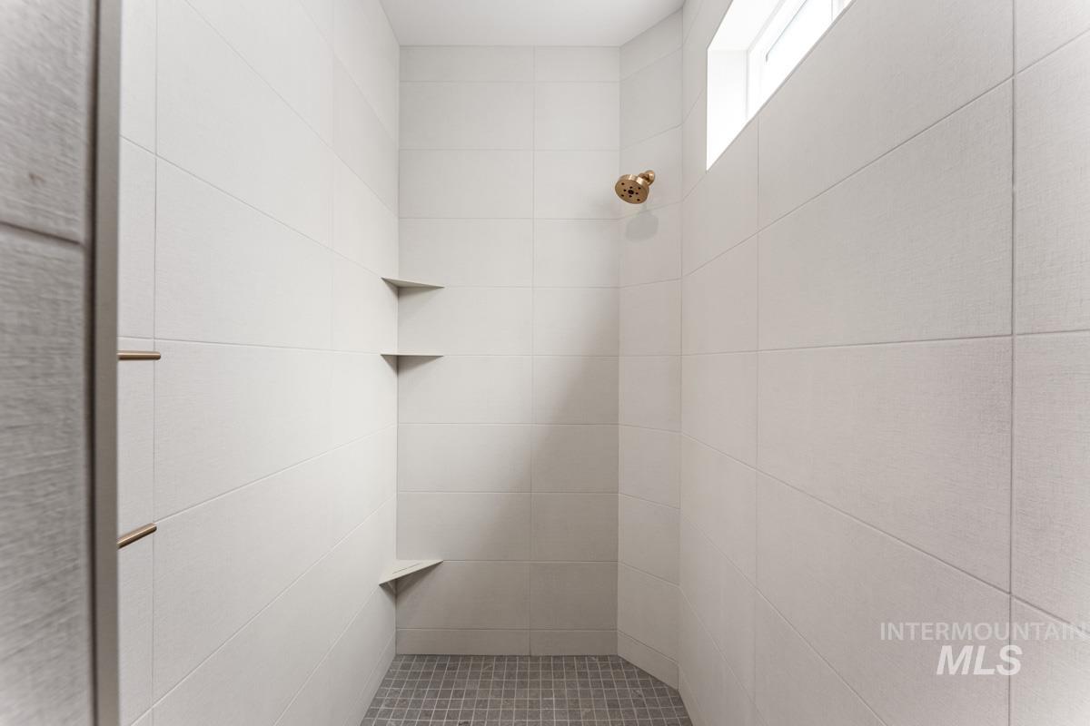 Shower enclosure featuring large format white wall tiles, a bronze-finish showerhead, three built-in corner shelves, and a dark tile mosaic floor