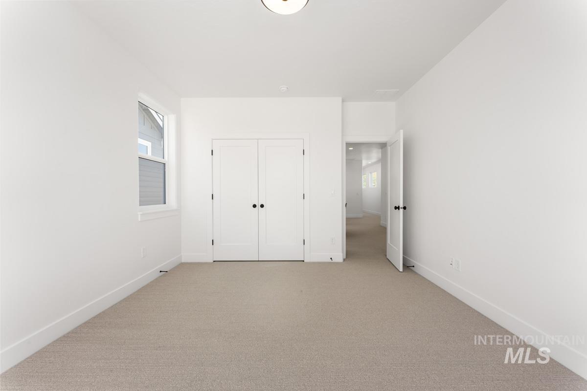 Bright room featuring neutral carpeting, white walls, a single window, and a double-door closet with black hardware