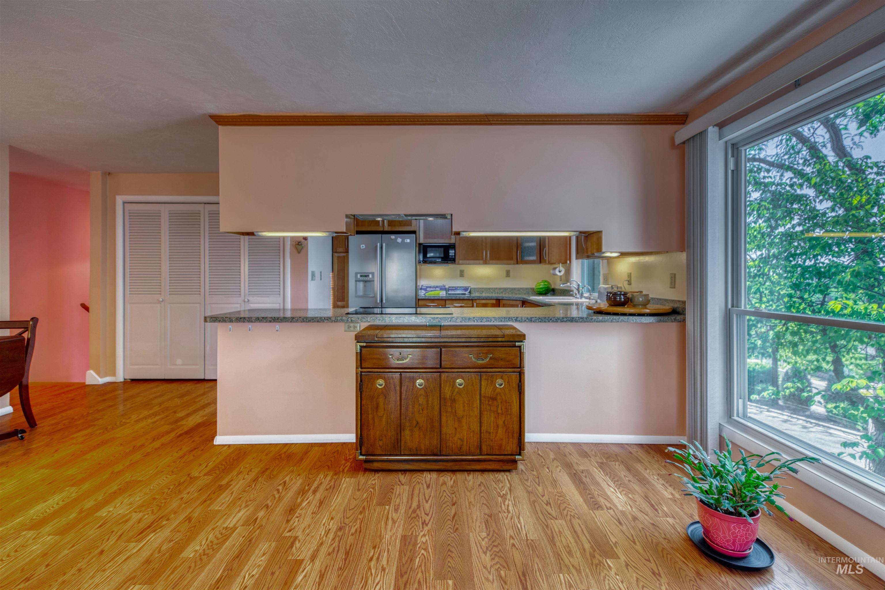 Kitchen with a peninsula, brown cabinets, light wood-style floors, stainless steel fridge with ice dispenser, and black microwave