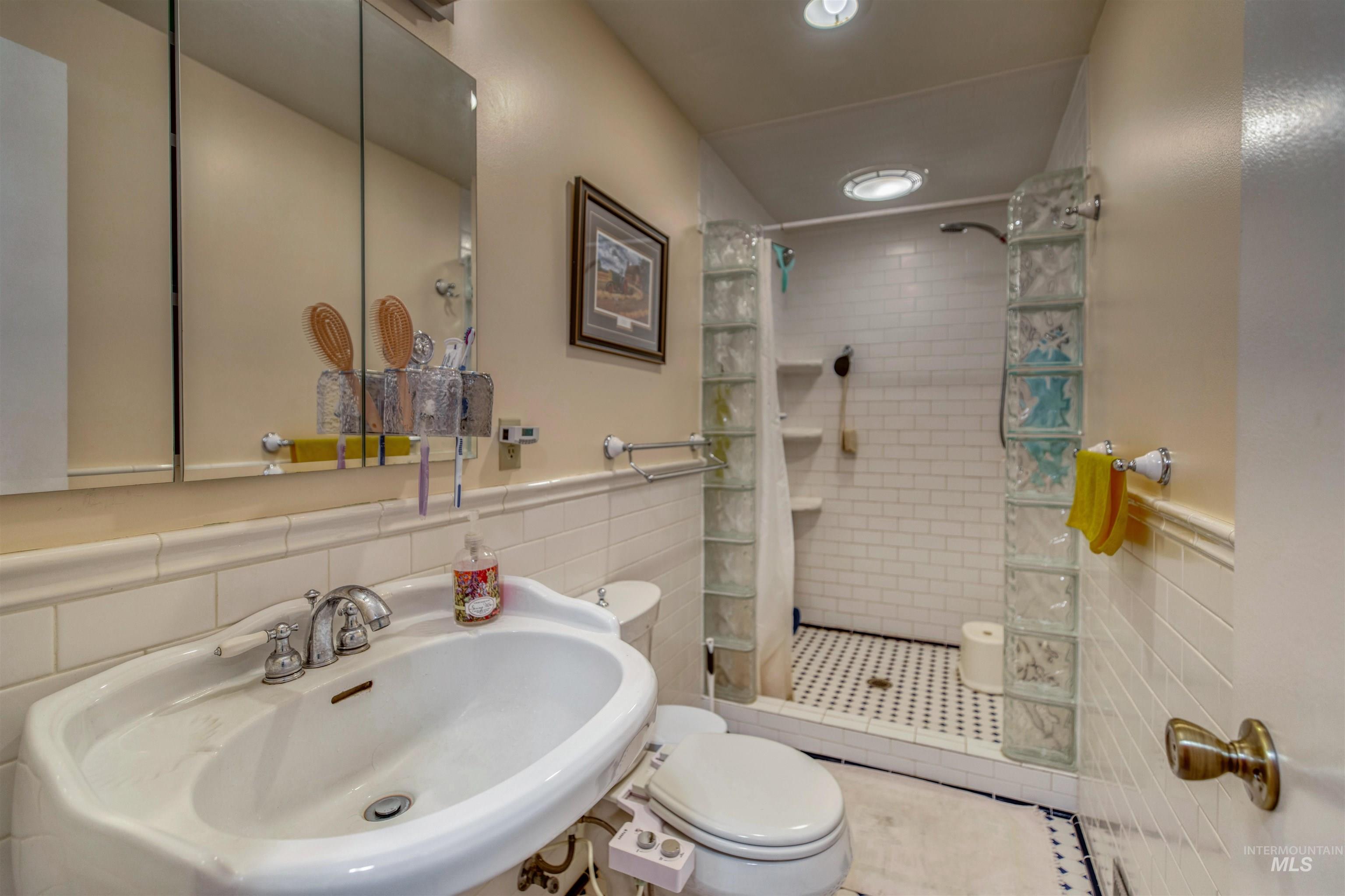 Full bathroom featuring wainscoting, tile walls, and tiled shower