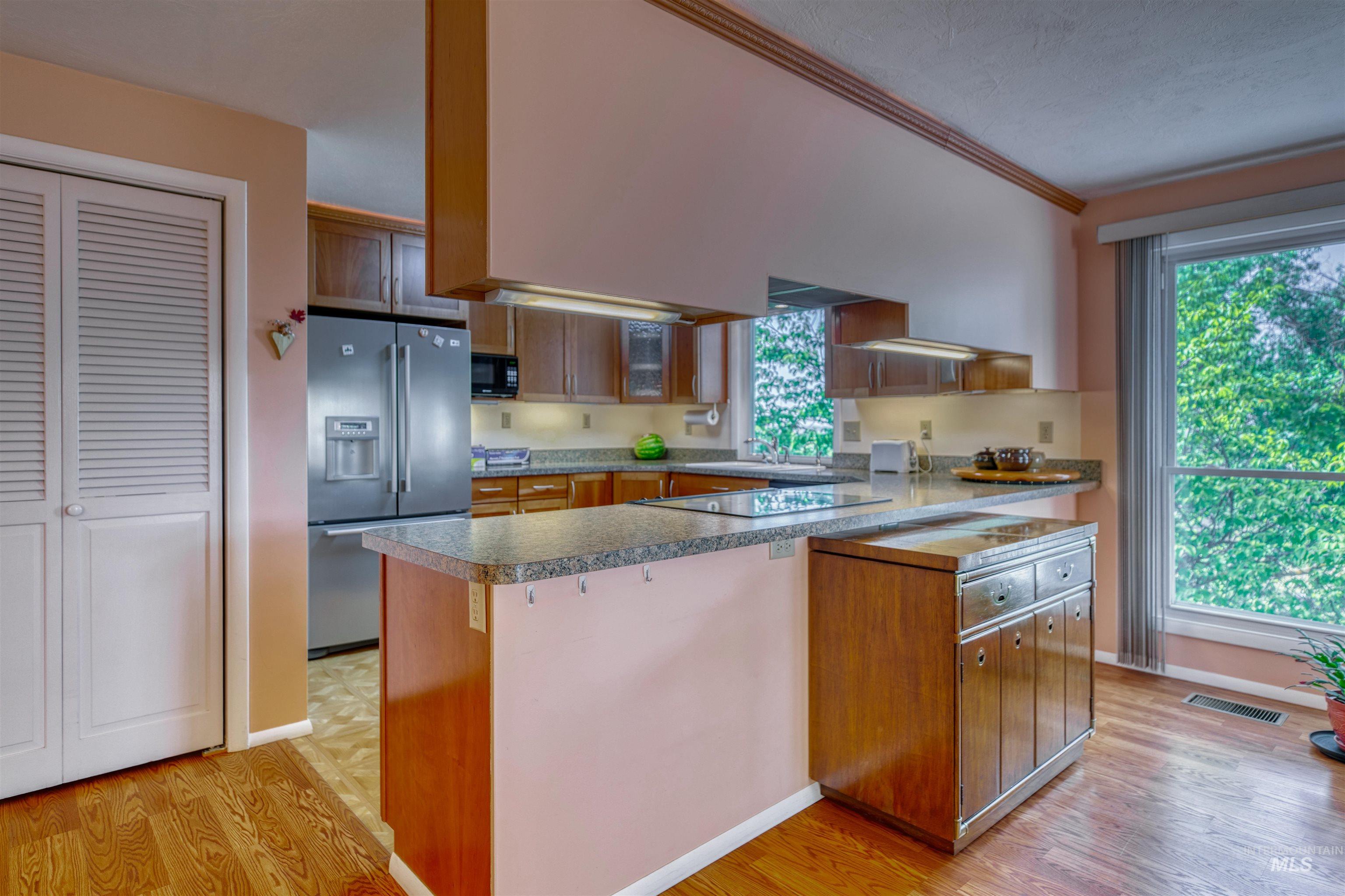 Kitchen featuring brown cabinets, black appliances, light wood-style flooring, a peninsula, and ornamental molding