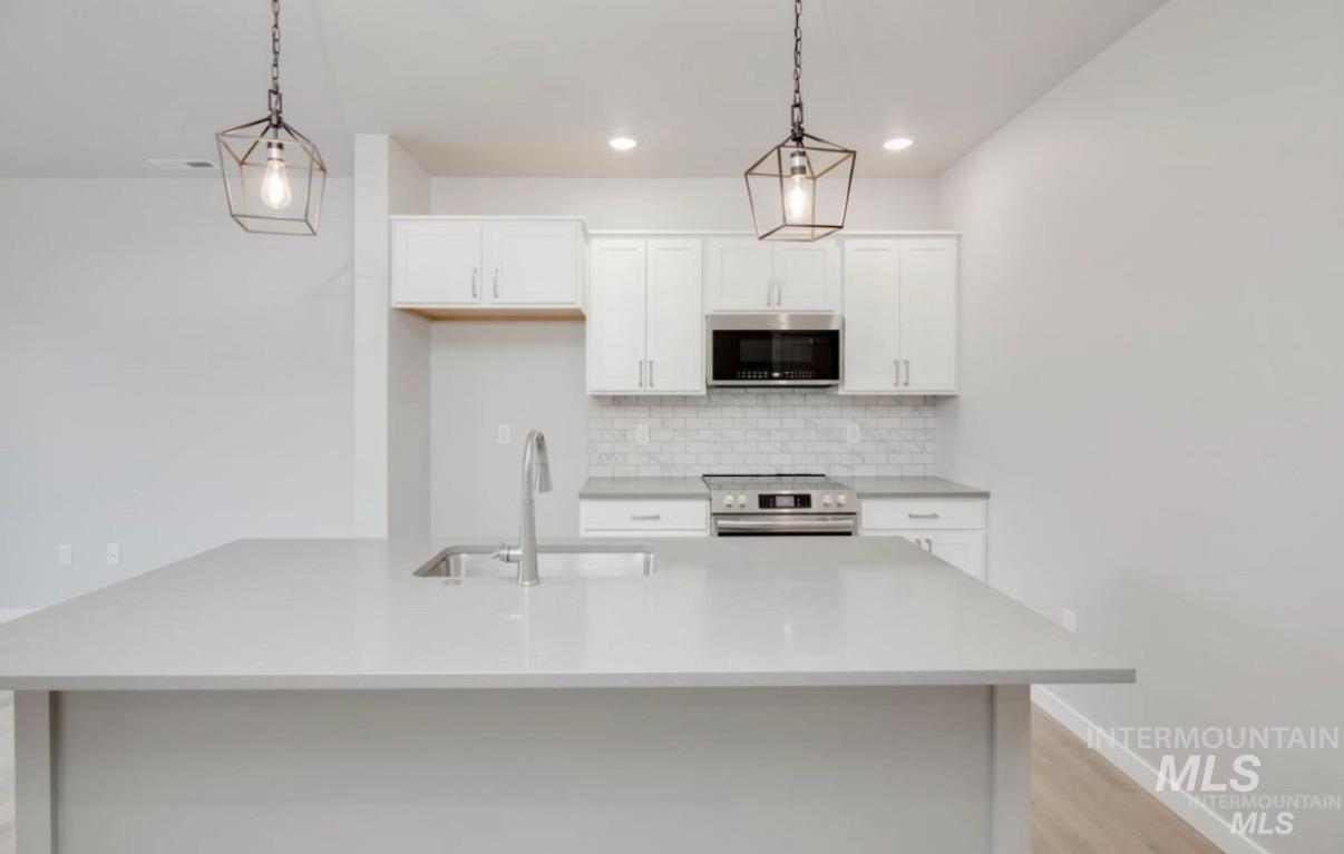 Kitchen featuring stainless steel appliances, white cabinets, pendant lighting, decorative backsplash, and light wood-type flooring