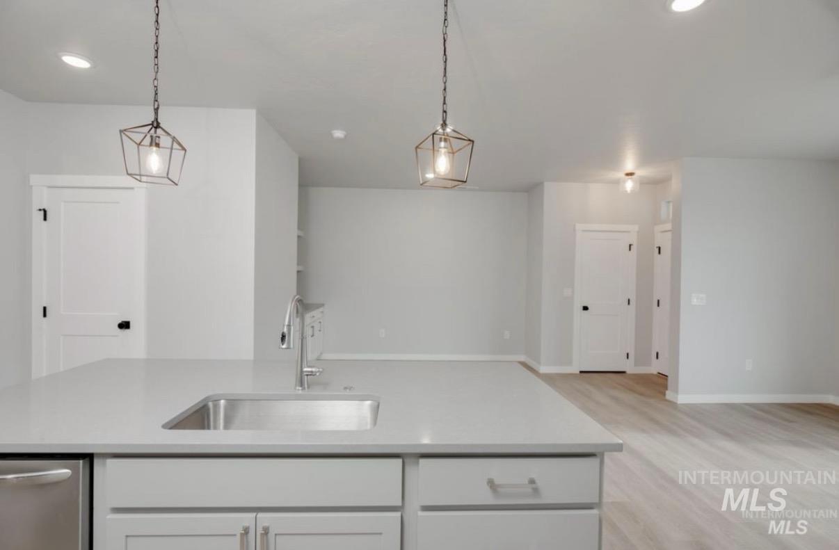 Kitchen featuring light wood-style flooring, hanging light fixtures, a center island with sink, light stone countertops, and open floor plan