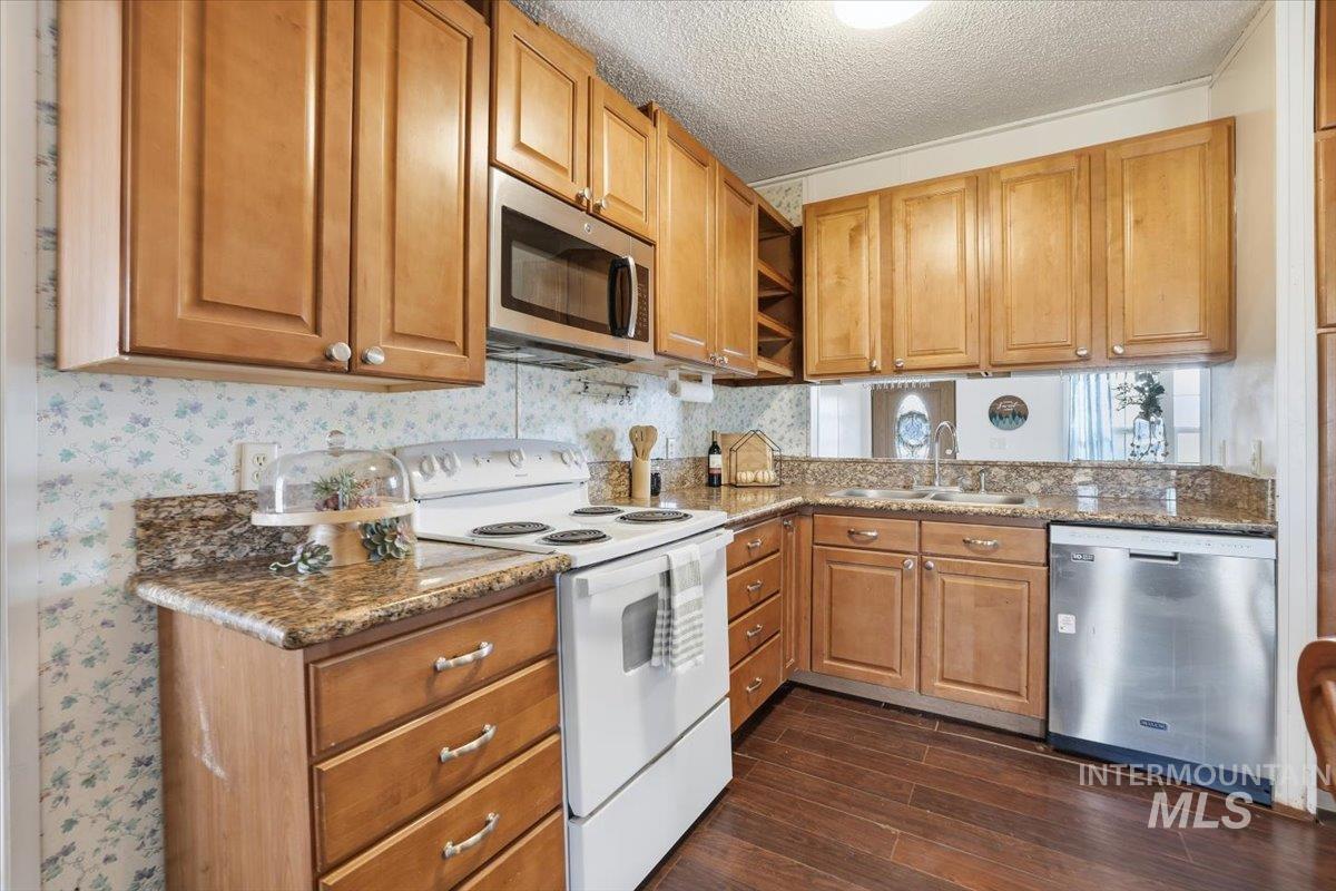 Kitchen featuring appliances with stainless steel finishes, a textured ceiling, brown cabinetry, dark wood-type flooring, and dark stone countertops