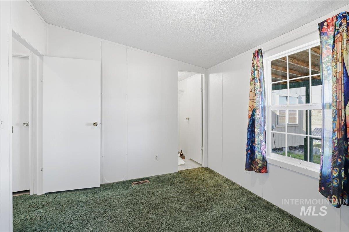 Unfurnished bedroom featuring carpet, a textured ceiling, and vaulted ceiling