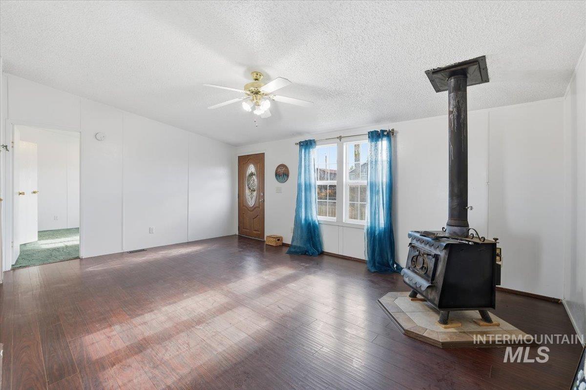 Unfurnished living room featuring a wood stove, a textured ceiling, dark wood finished floors, and a ceiling fan